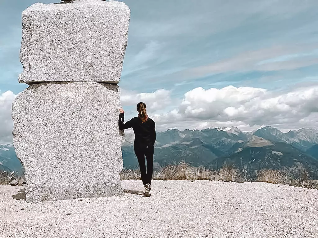 Frau genießt den Ausblick auf die Berge und lehnt sich an einem Steingebilde an